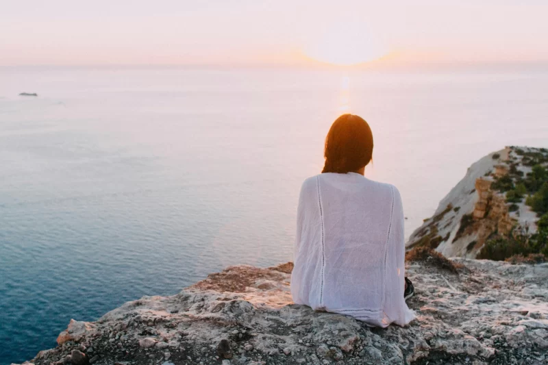 a imagem mostra uma mulher sentada meditando em frente ao mar para se conectar com a criança interior