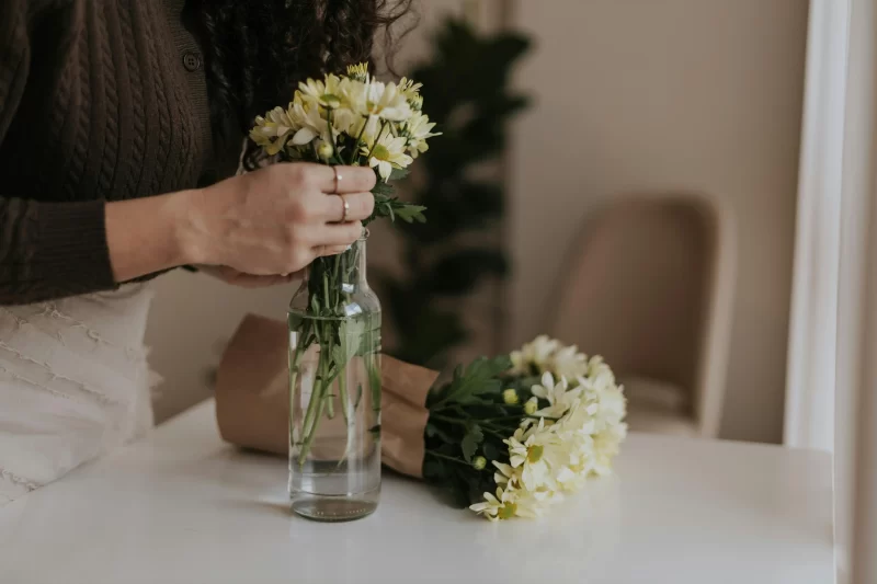 a imagem mostra uma mulher colocando flores em um jarro com água com a intenção de ter um final de semana cozy em casa e descansar