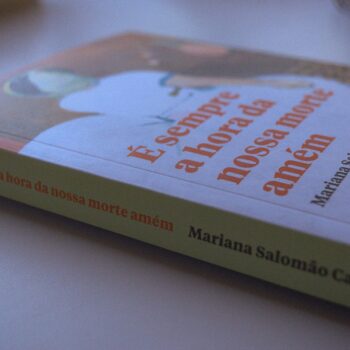 a imagem mostra o livro É sempre a hora da nossa morte amém, da escritora Mariana Salomão Carrara, em cima de uma mesa
